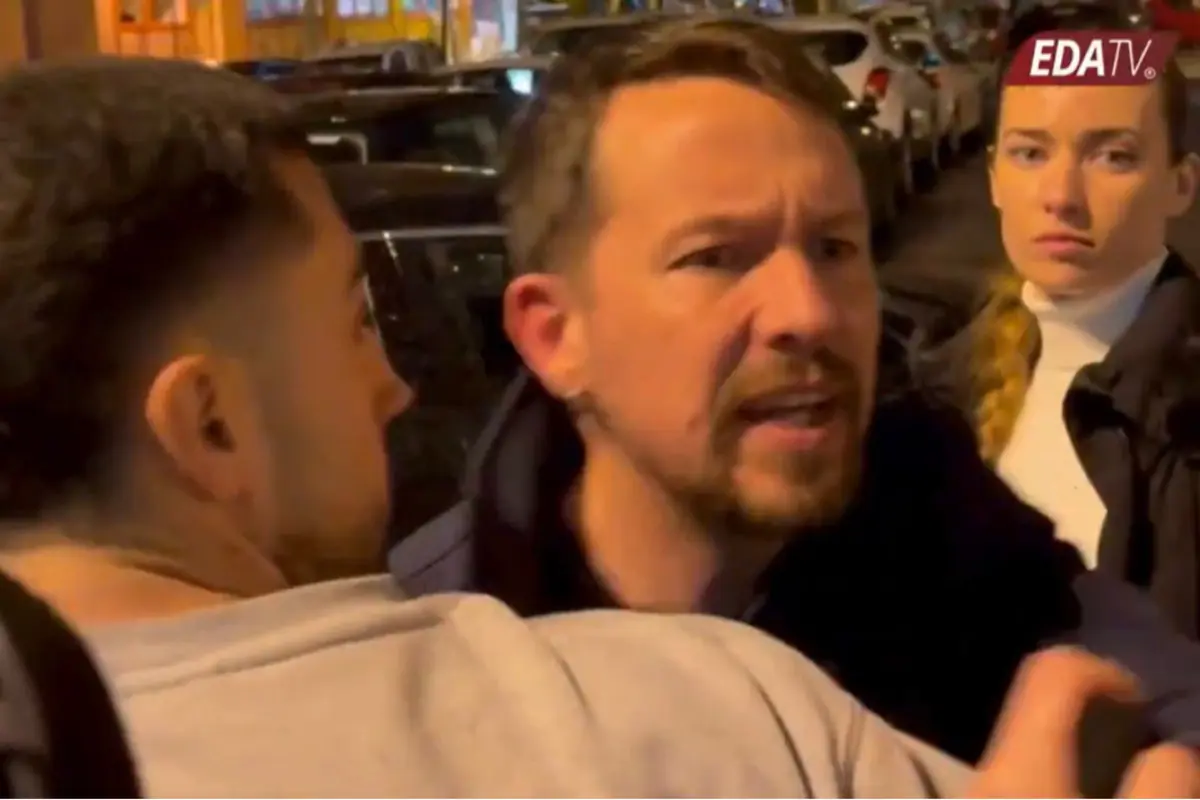 Tres personas discuten en una calle de noche mientras un hombre con barba es sujetado por otro y una mujer observa seria al fondo