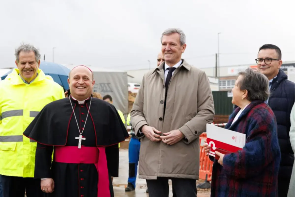 Grupo de personas sonrientes en un acto público al aire libre con un obispo vestido con sotana negra y faja rosa junto a varios representantes civiles con ropa de abrigo