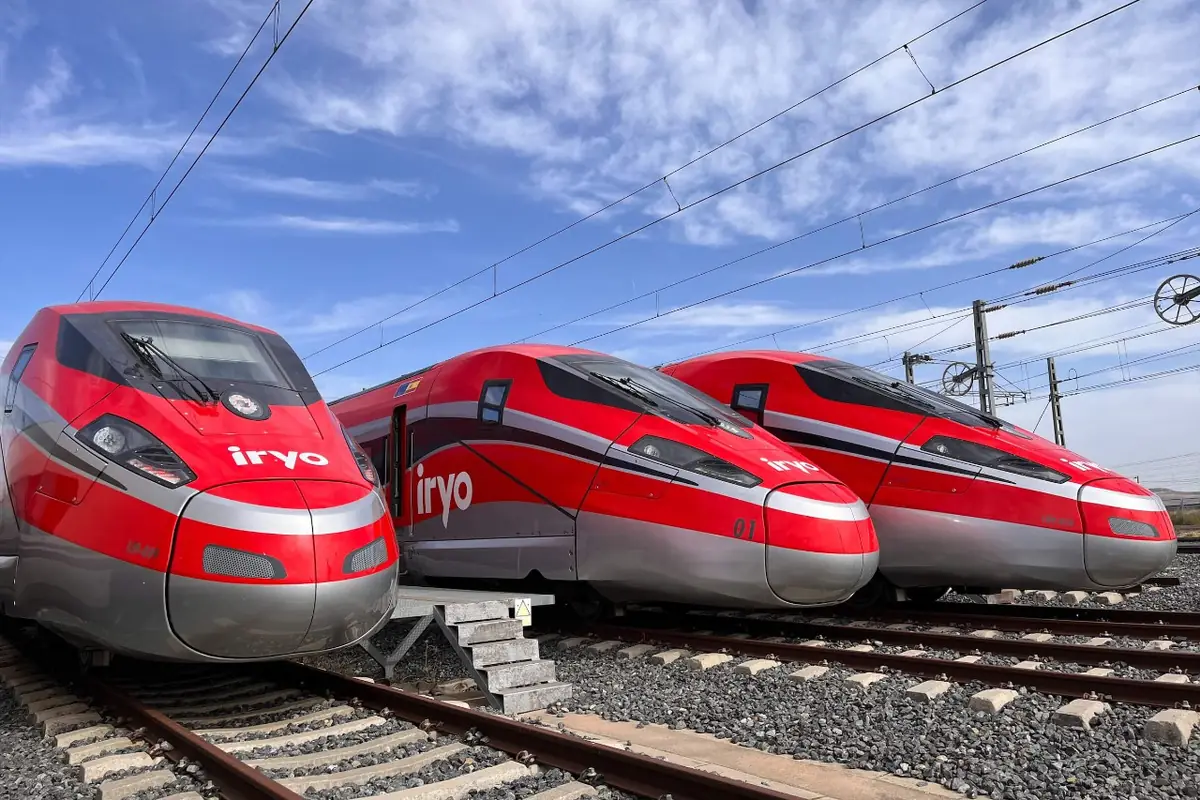 Tres trenes de alta velocidad rojos de la compañía iryo alineados sobre las vías bajo un cielo azul con nubes
