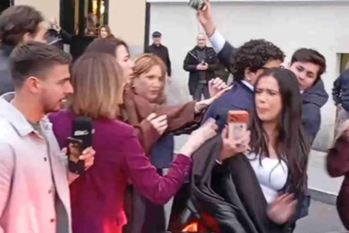 Grupo de personas discutiendo y empujándose en la calle mientras una reportera con micrófono y varios móviles graban la escena