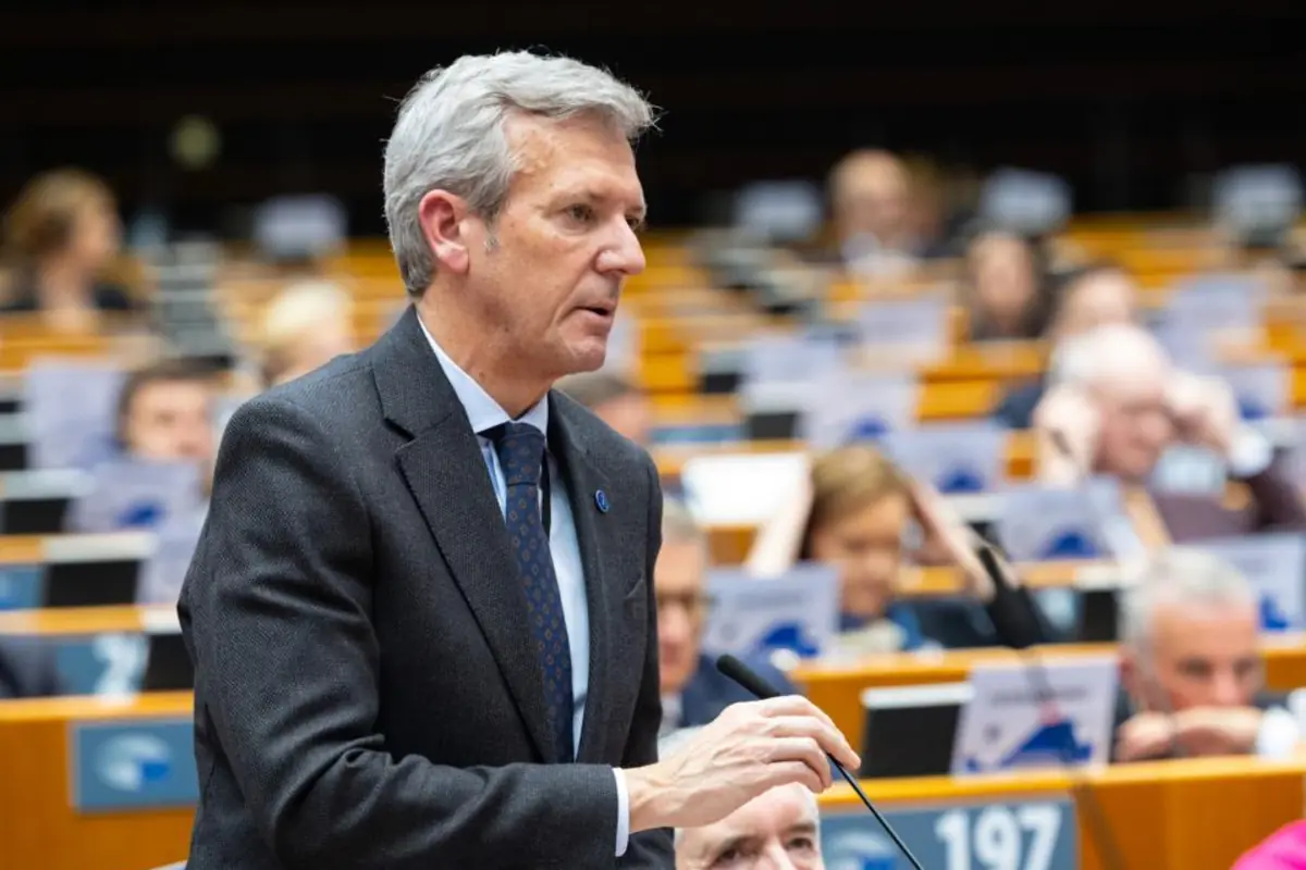 Hombre de cabello canoso con traje oscuro hablando frente a un micrófono en una sala de conferencias llena de asistentes