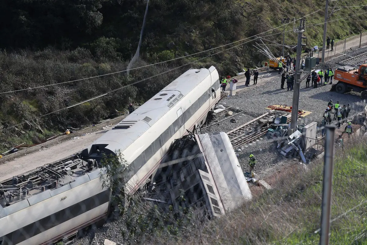 Tren descarrilado con varios vagones volcados junto a la vía mientras equipos de emergencia y maquinaria pesada trabajan en la zona del accidente