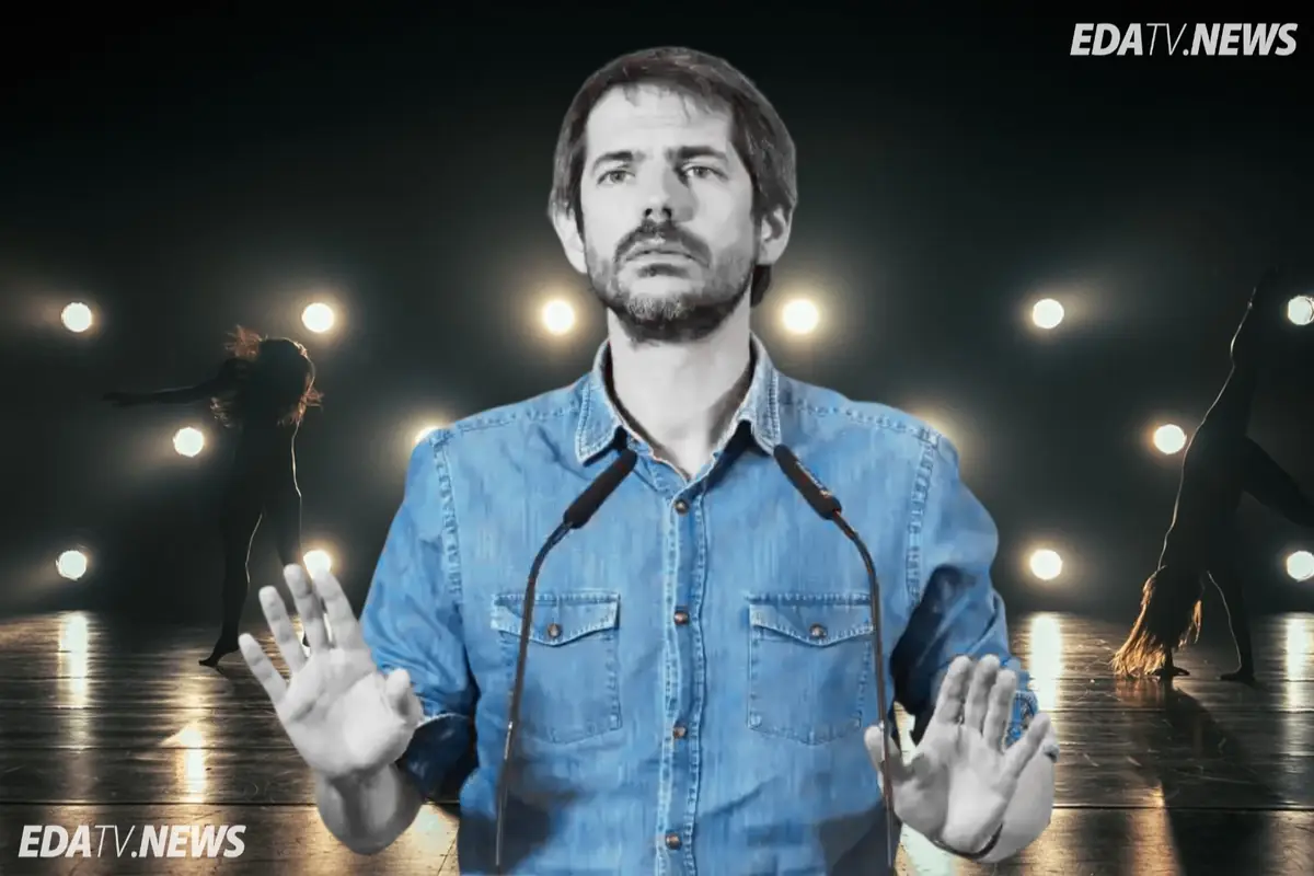 Hombre con camisa vaquera hablando ante micrófonos sobre un escenario oscuro con focos encendidos y siluetas de bailarinas al fondo