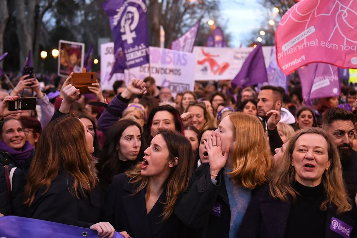 Multitud de personas en una manifestación feminista al aire libre con pancartas y banderas moradas mientras corean consignas y levantan el puño Multitud de personas en una manifestación feminista al aire libre con pancartas y banderas moradas mientras corean consignas y levantan el puño