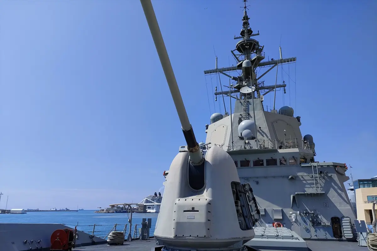 Cañón naval en la cubierta de un buque de guerra moderno atracado en un puerto con cielo despejado