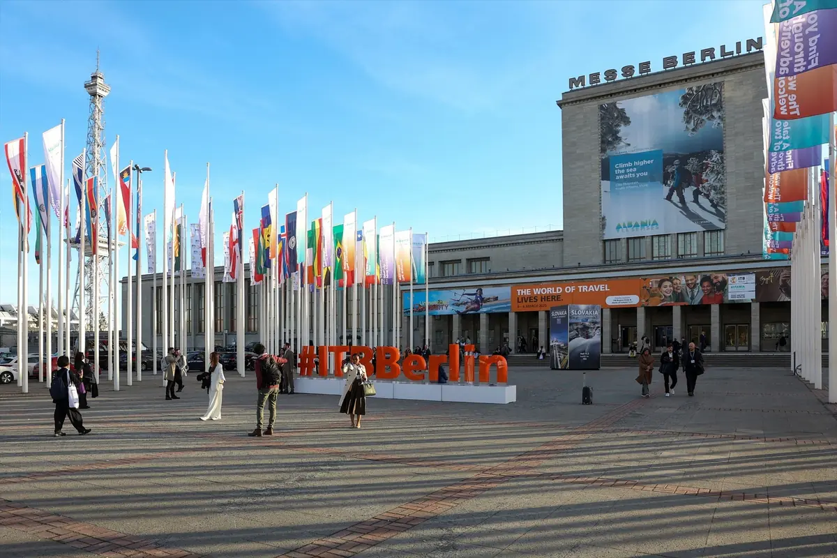 Entrada principal de Messe Berlin con numerosas banderas de distintos países y un gran letrero naranja con el texto ITB Berlin en el centro de la plaza