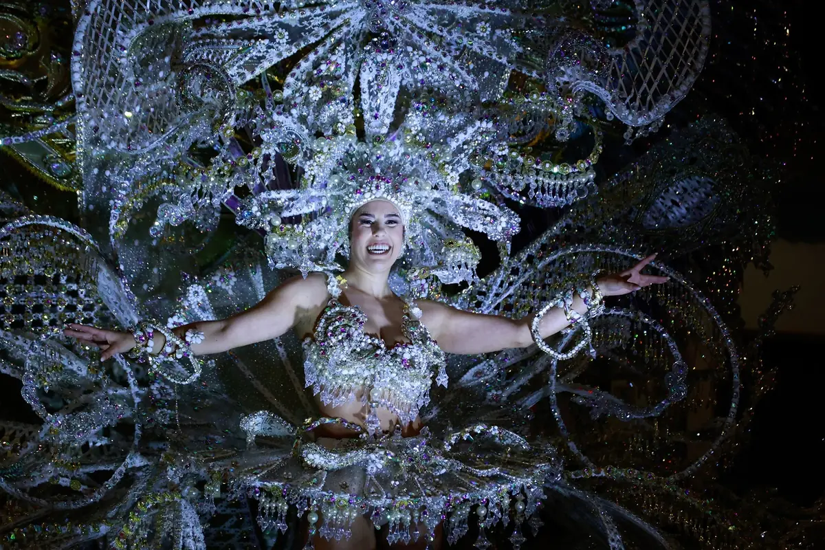 Bailarina de carnaval sonriendo con un elaborado traje brillante lleno de pedrería y plumas en un desfile nocturno