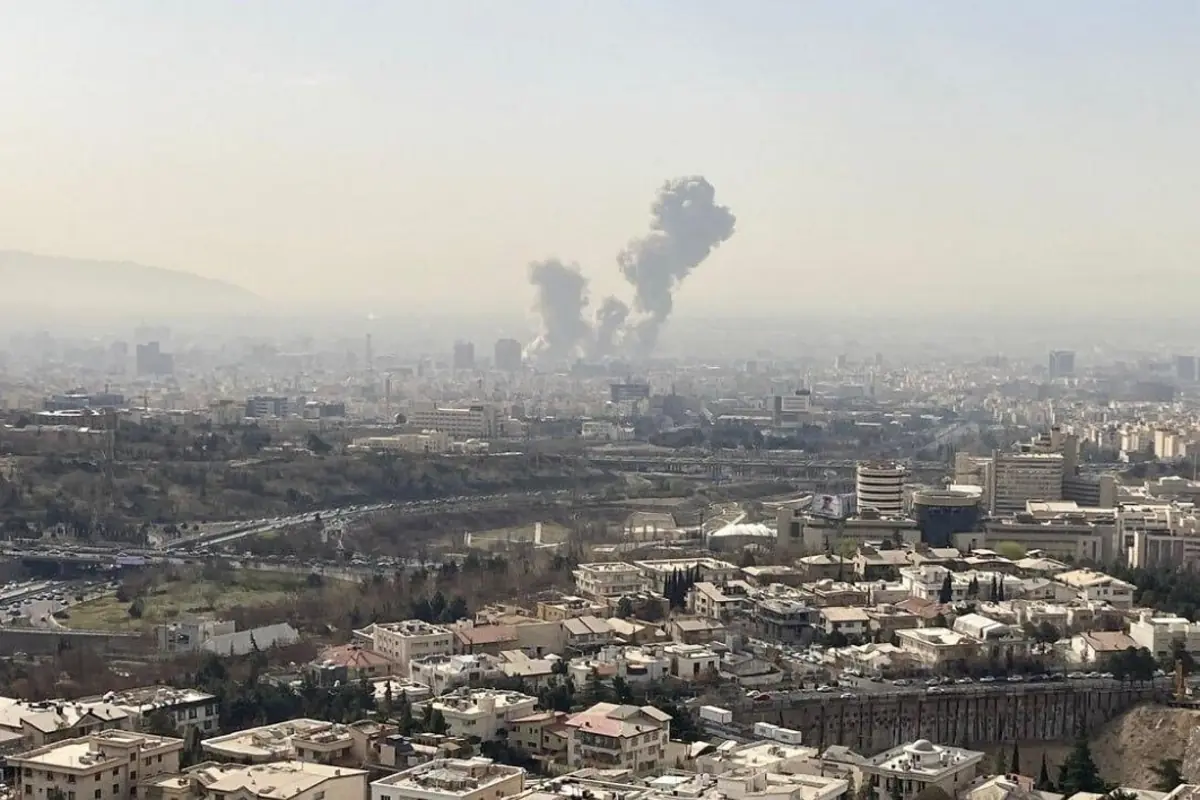 Vista panorámica de una ciudad con columnas de humo elevándose en la distancia sobre la zona urbana