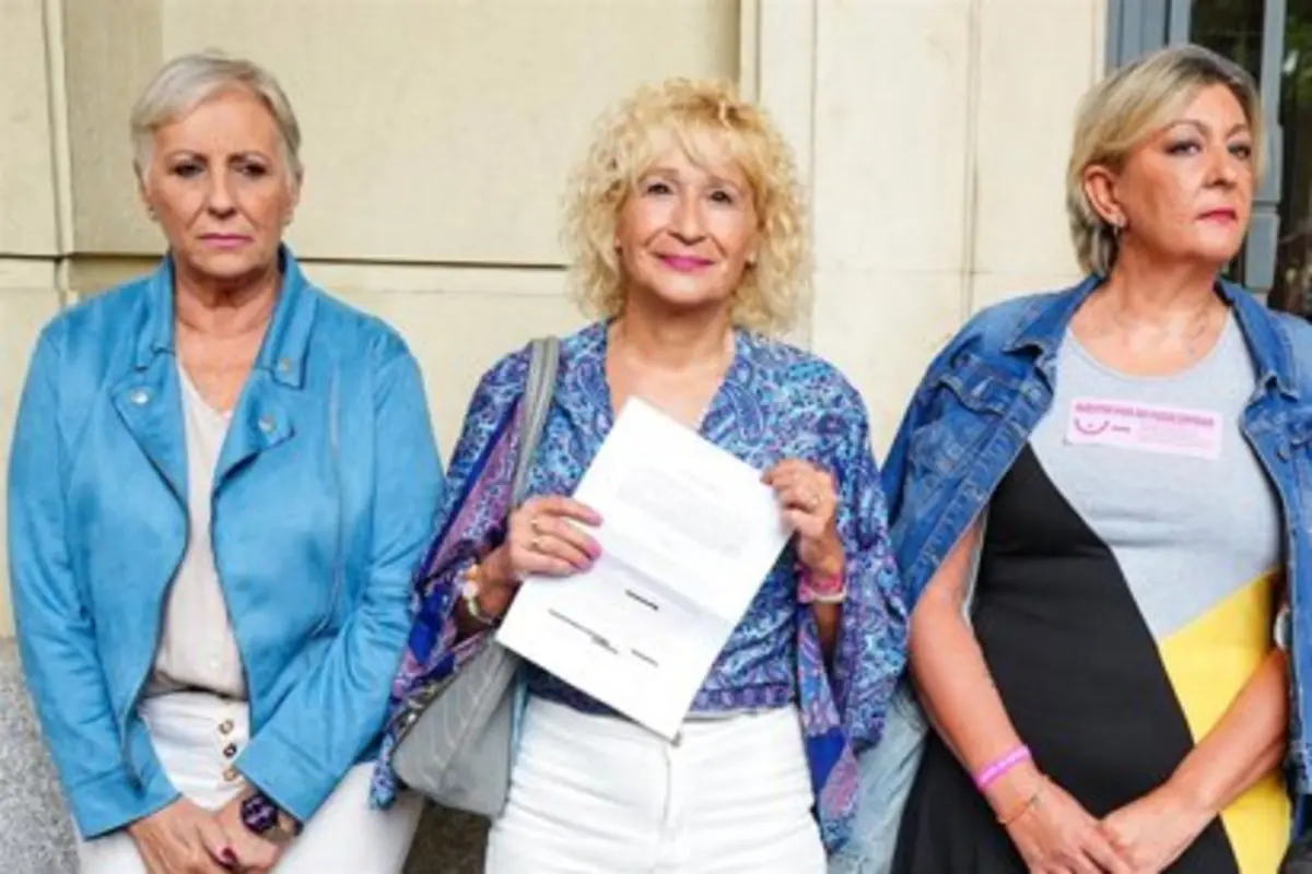 Tres mujeres adultas posan de pie frente a un edificio la del centro sostiene unos documentos en las manos
