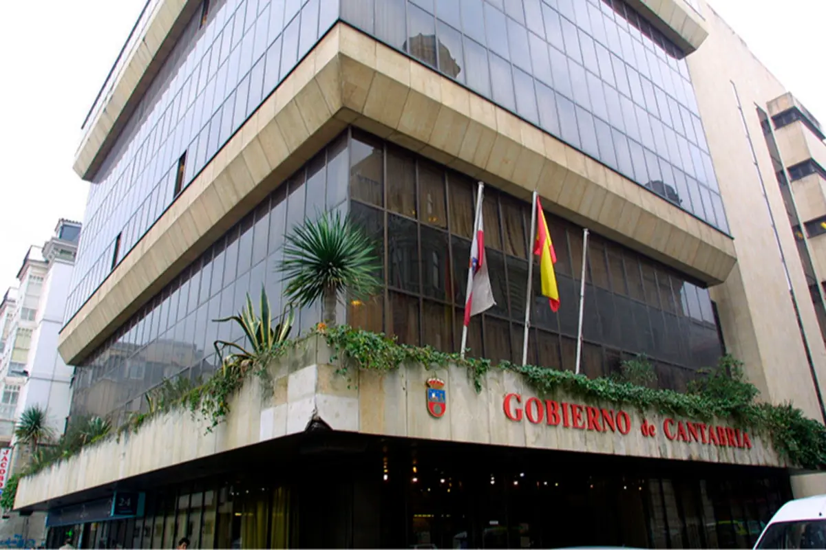 Fachada del edificio del Gobierno de Cantabria con grandes ventanales banderas en mástiles y vegetación en la cornisa