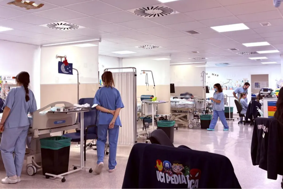 Personal sanitario trabajando en una unidad de cuidados intensivos pediátricos con varias camas, equipos médicos y niños pacientes en un espacio hospitalario amplio y luminoso