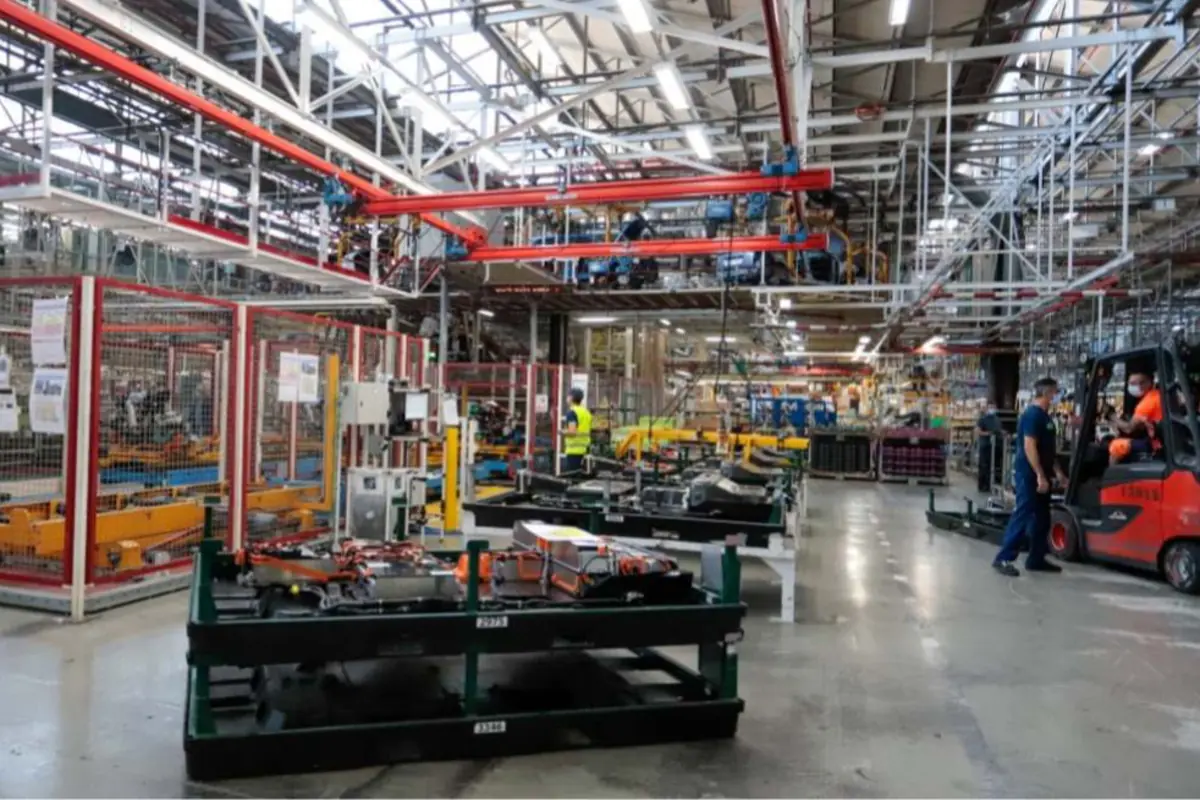 Planta industrial con líneas de montaje automatizadas y trabajadores operando maquinaria y montacargas