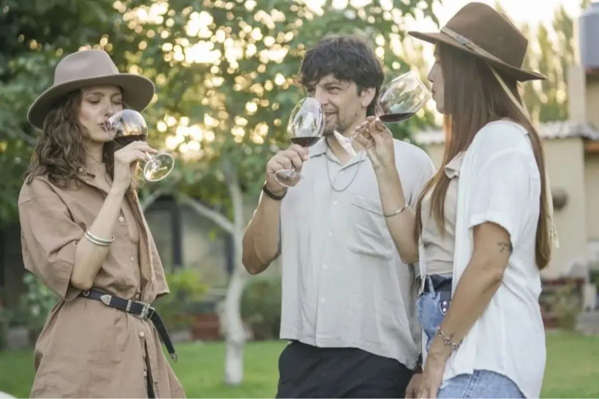 Tres personas jóvenes al aire libre brindando y degustando copas de vino tinto en un jardín al atardecer Tres personas jóvenes al aire libre brindando y degustando copas de vino tinto en un jardín al atardecer
