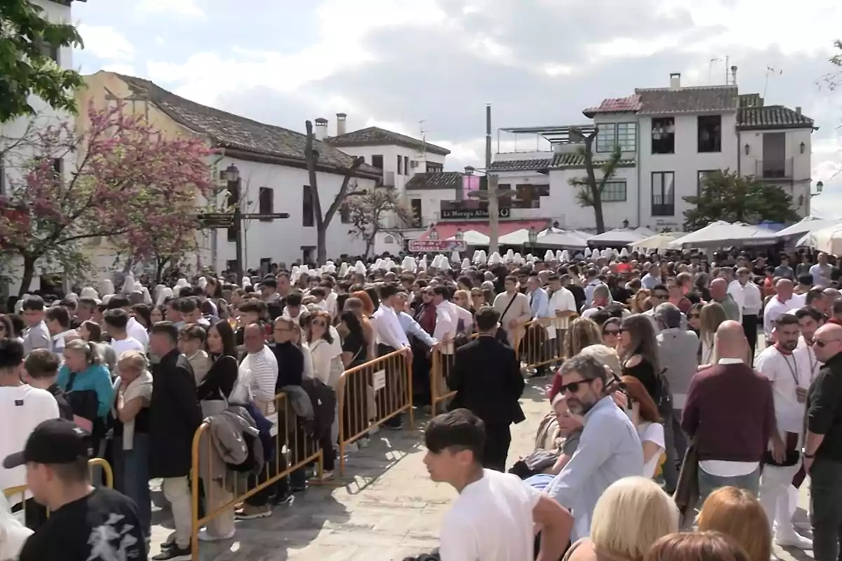 Una multitud de personas se reúne en una plaza al aire libre, rodeada de edificios tradicionales y árboles en flor, con un cielo parcialmente nublado. Una multitud de personas se reúne en una plaza al aire libre, rodeada de edificios tradicionales y árboles en flor, con un cielo parcialmente nublado.