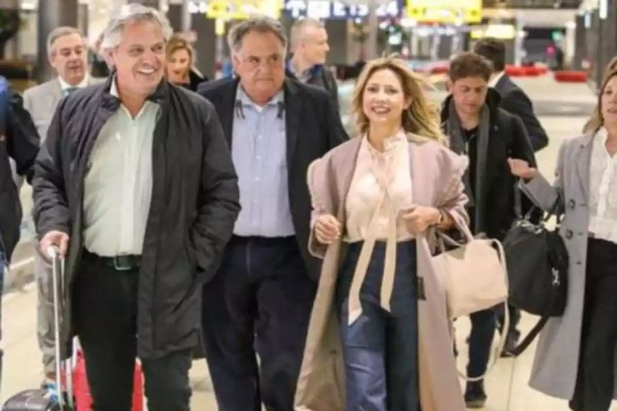 Un grupo de personas camina por un aeropuerto, algunas de ellas llevan equipaje y parecen estar conversando y sonriendo.
