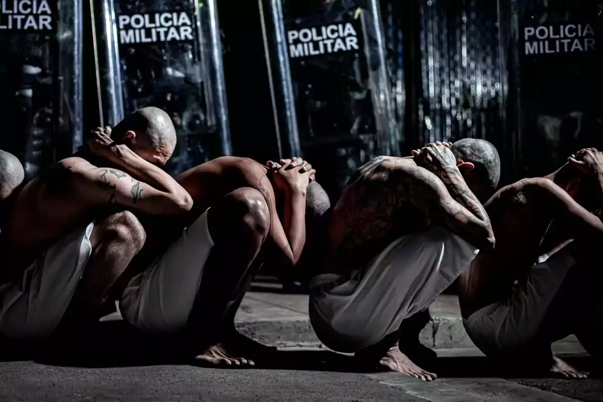 Hombres con la cabeza rapada y tatuajes, agachados con las manos en la cabeza, frente a escudos de la policía militar.