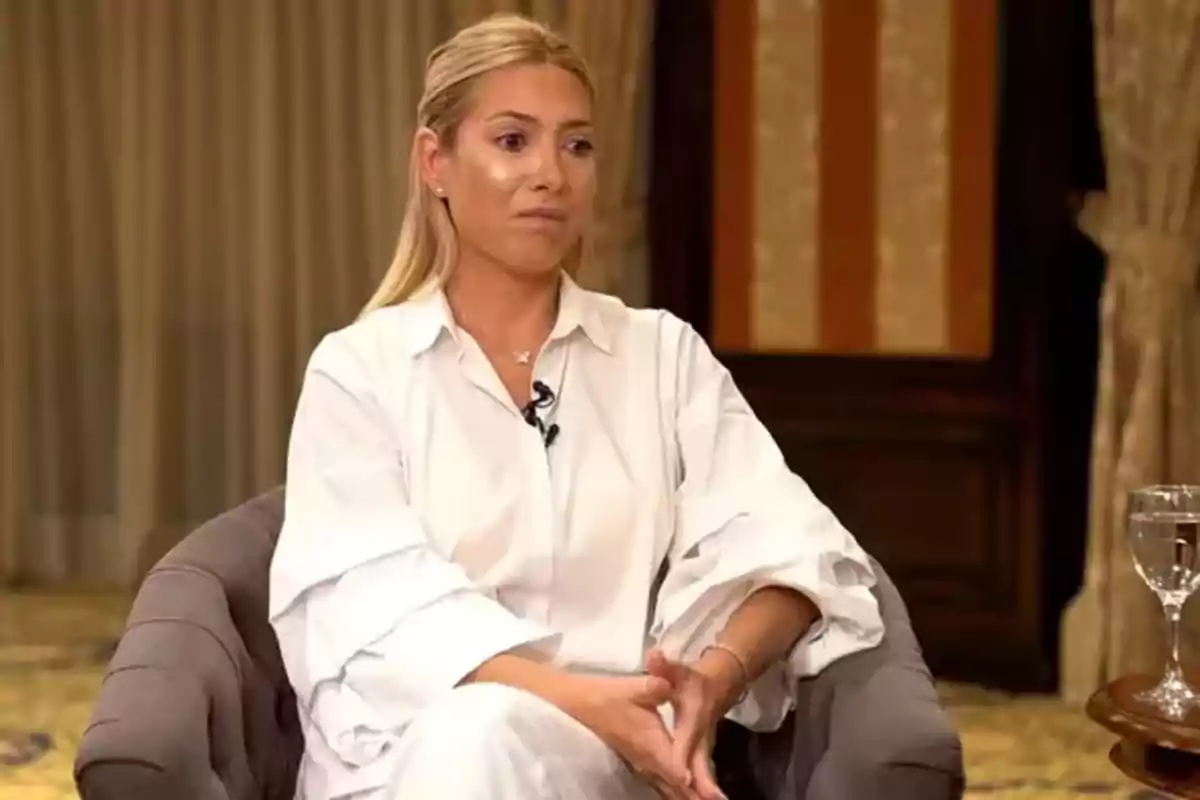 Mujer sentada en una silla durante una entrevista, con una camisa blanca y el cabello recogido.