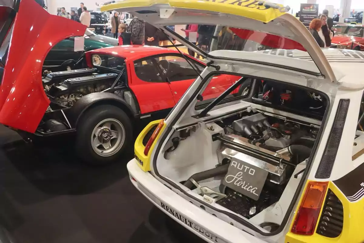 Dos autos clásicos con los compartimentos del motor abiertos en una exhibición de automóviles, rodeados de personas observando.