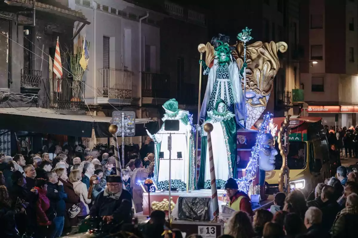 A float decorated with figures dressed in green and white moves down a street full of spectators during a nighttime parade.