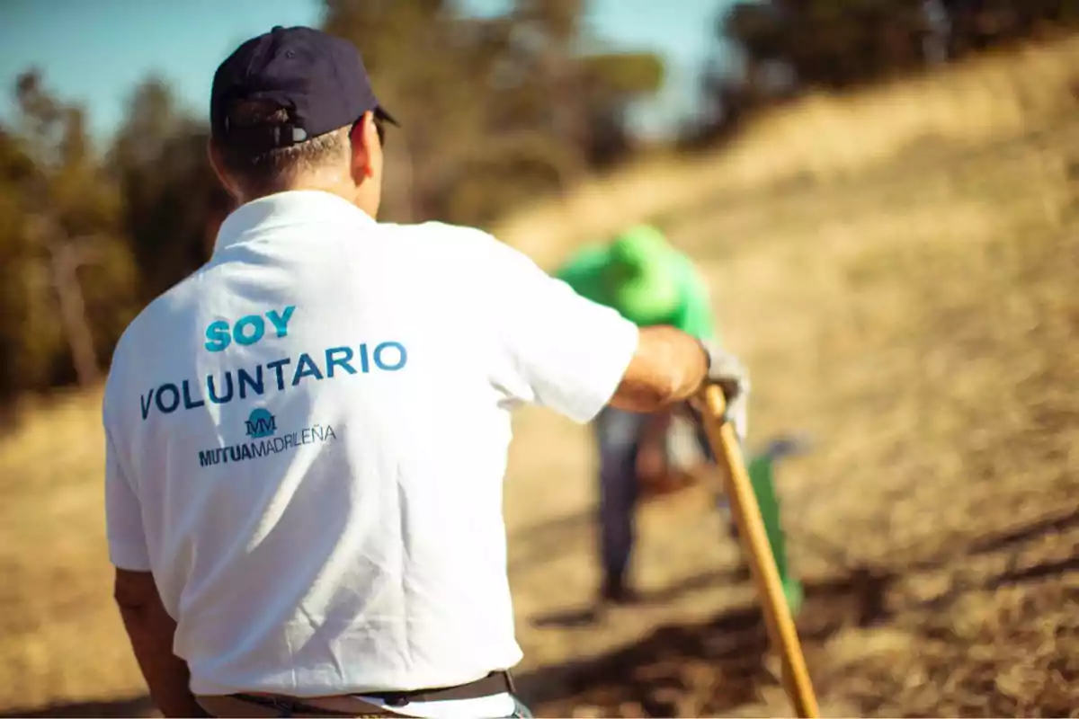 Hombre con camiseta blanca de voluntario trabajando al aire libre en un campo junto a otra persona