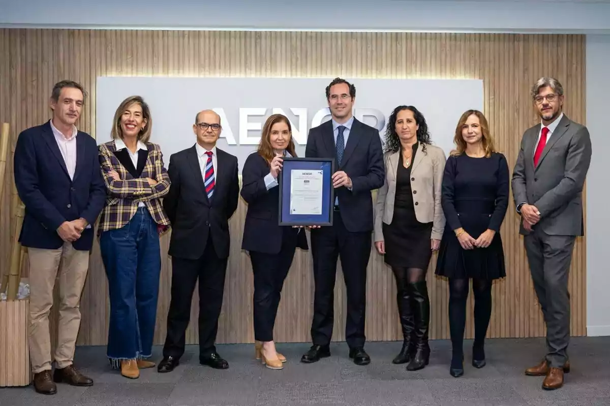 Un grupo de personas posando juntas en una oficina mientras sostienen un certificado enmarcado.