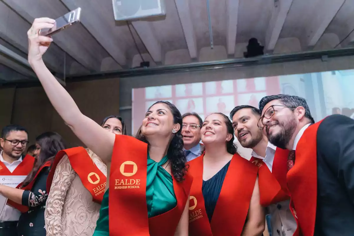 Un grupo de personas con estolas rojas de la EALDE Business School se toman una selfie en un evento.