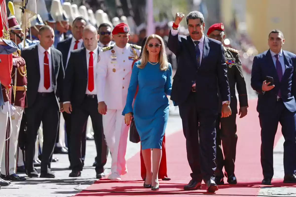 Un grupo de personas camina por una alfombra roja, algunas de ellas con uniformes militares y otras con trajes formales.