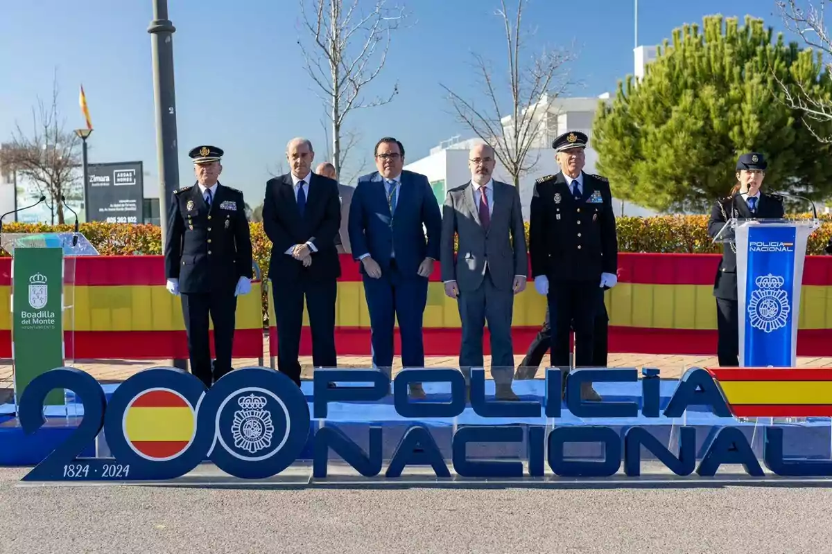 A group of people in uniform and suits pose in front of a sign that says "National Police" with a Spanish flag and the dates 1824-2024 at an outdoor event in Boadilla del Monte.