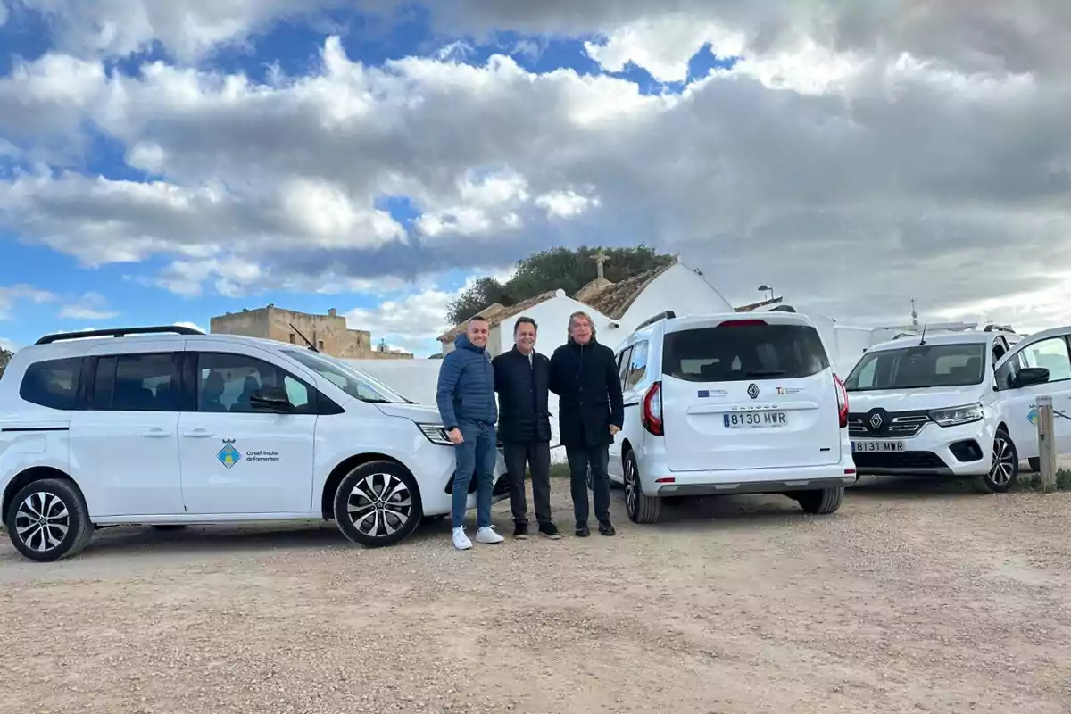 Tres personas posan junto a tres vehículos blancos en un entorno rural con cielo nublado.