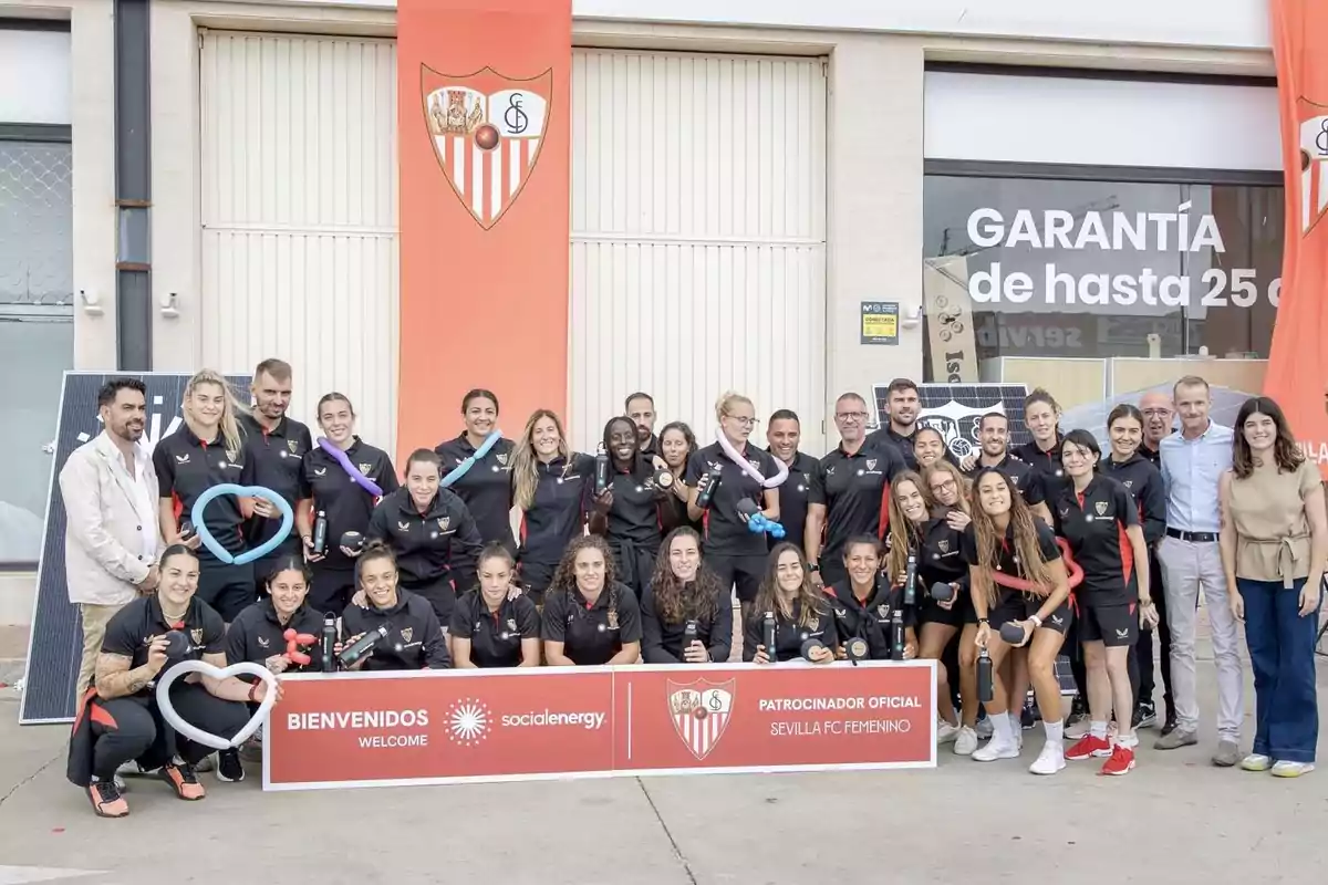 Un grupo de personas posando frente a un edificio con un cartel que dice "Bienvenidos" y "Patrocinador Oficial Sevilla FC Femenino".