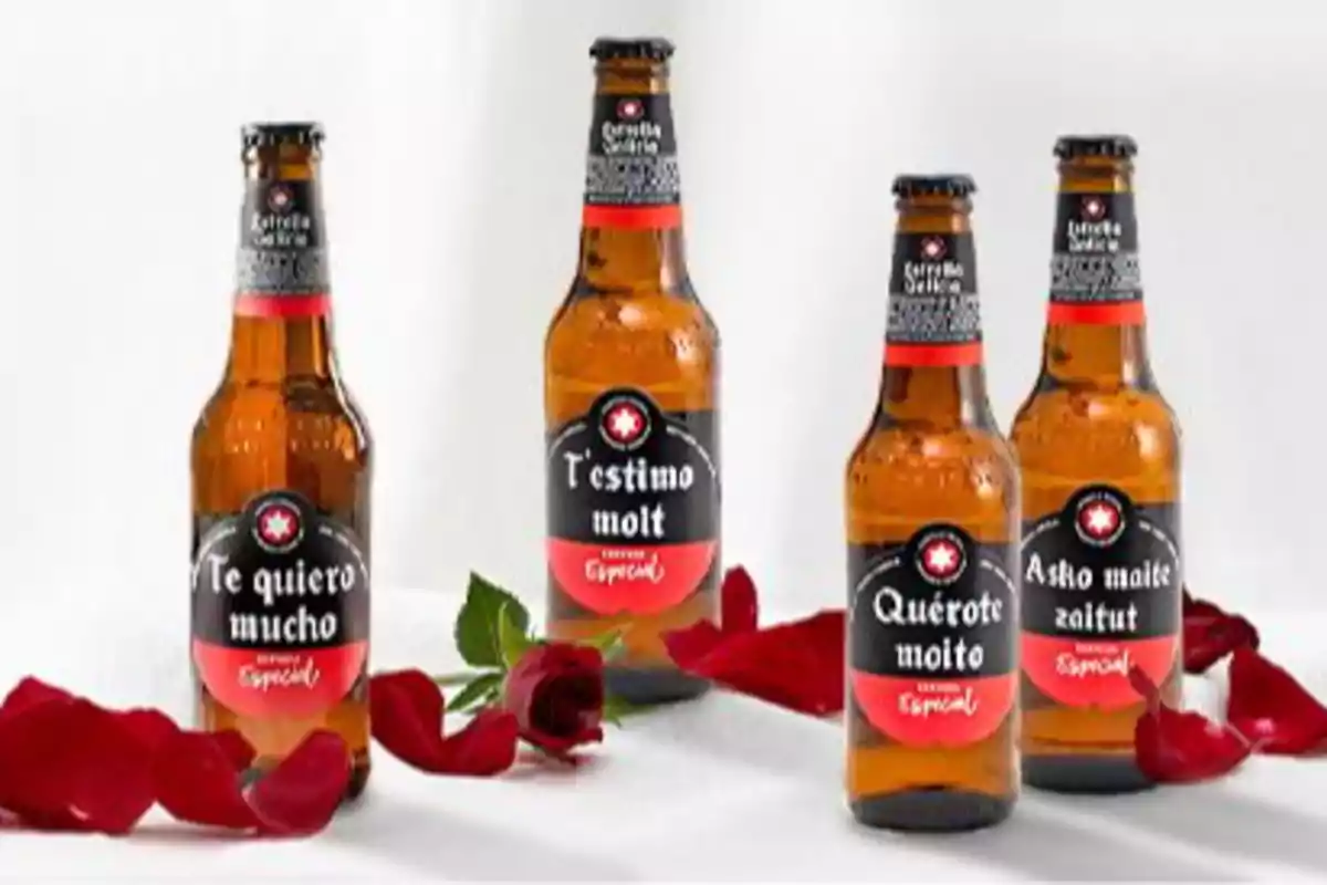 Cuatro botellas de cerveza con etiquetas que dicen "Te quiero mucho" en diferentes idiomas rodeadas de pétalos de rosa.