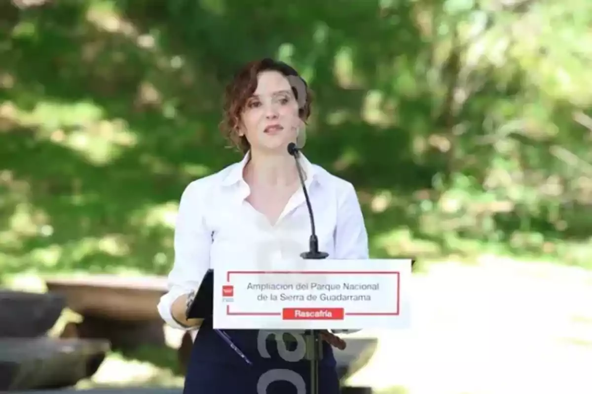 Una mujer hablando en un podio con un cartel que dice "Ampliación del Parque Nacional de la Sierra de Guadarrama, Rascafría" en un entorno al aire libre.