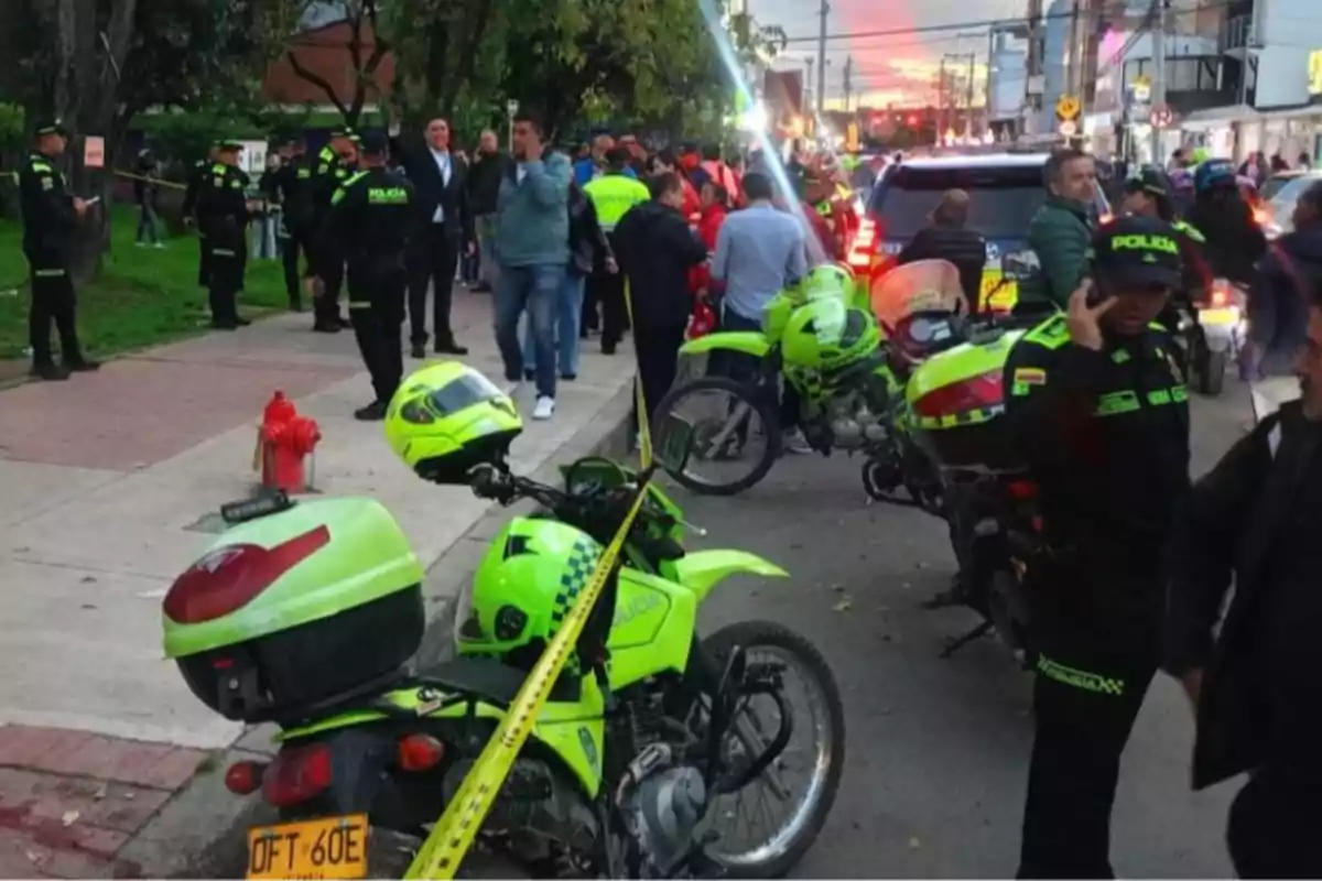 Varios policías y motos oficiales rodean una zona acordonada en una calle mientras varias personas observan la escena Varios policías y motos oficiales rodean una zona acordonada en una calle mientras varias personas observan la escena