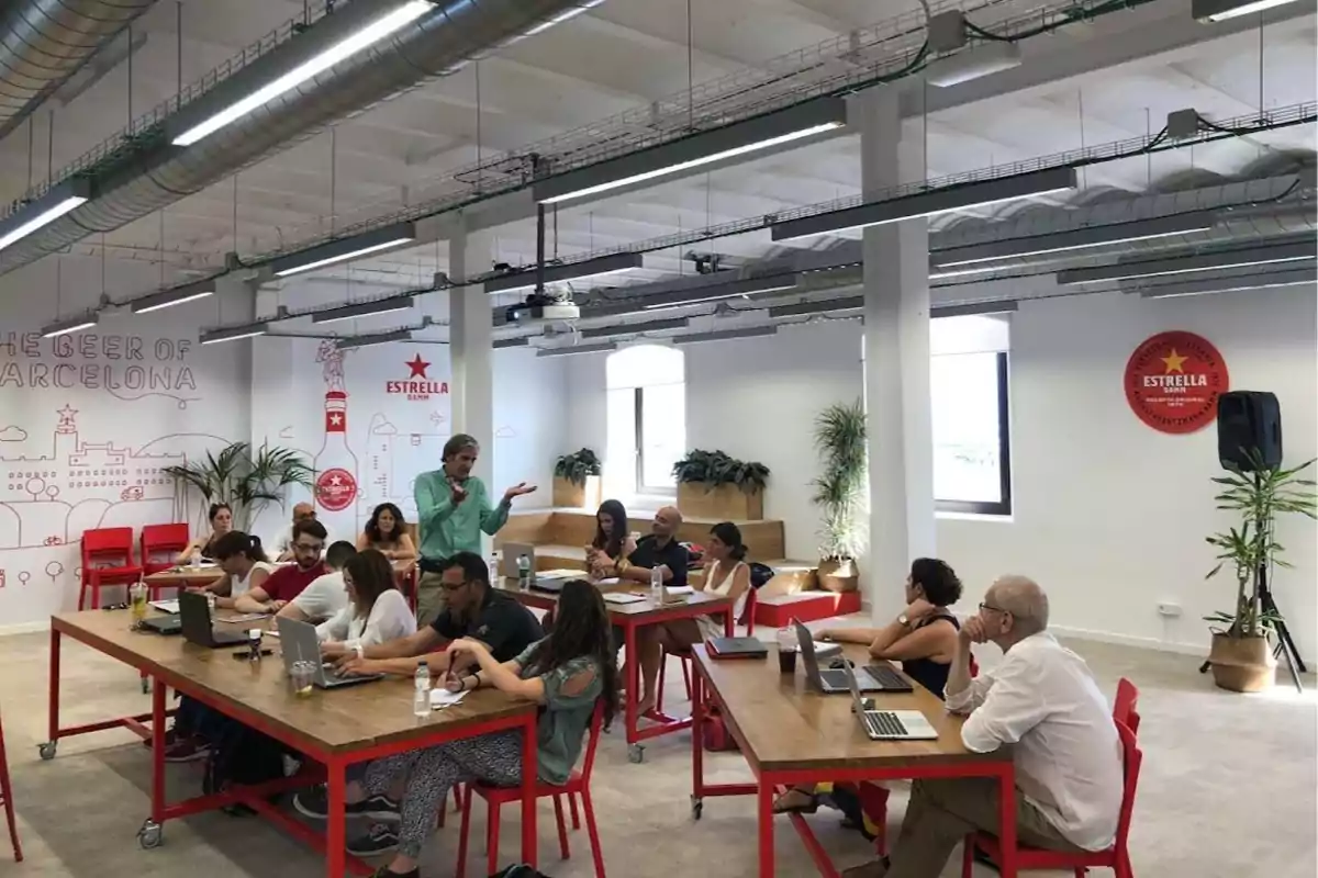 Personas trabajando en una oficina moderna con decoración de la marca Estrella Damm en las paredes.