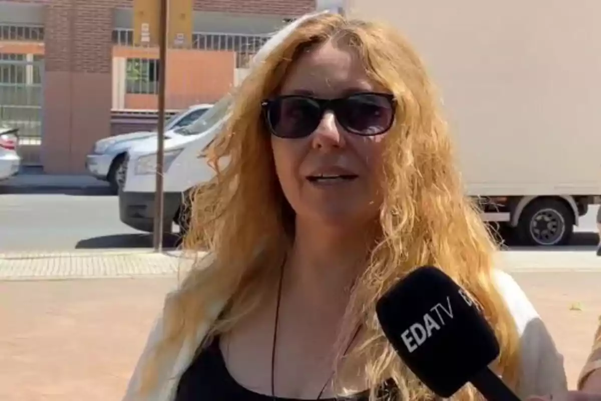 Mujer de cabello rubio y largo usando gafas de sol es entrevistada en la calle por un micrófono de EDA TV Mujer de cabello rubio y largo usando gafas de sol es entrevistada en la calle por un micrófono de EDA TV