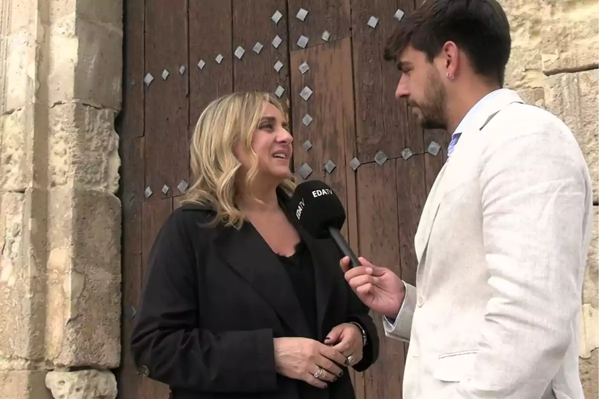 Una mujer siendo entrevistada por un hombre con micrófono frente a una puerta de madera. Una mujer siendo entrevistada por un hombre con micrófono frente a una puerta de madera.