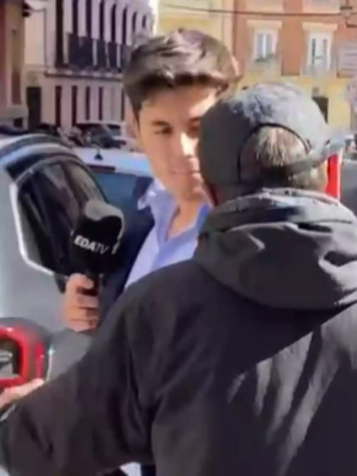 A reporter holds a microphone while talking to a man on the street.