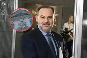 Un hombre de traje con barba y cabello corto sostiene documentos mientras camina frente a cámaras, con un recuadro que muestra la fachada del Tribunal Supremo.