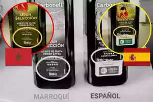 Dos botellas de aceite de oliva virgen extra de la marca Carbonell, una con etiqueta de origen marroquí y otra de origen español, con las banderas de Marruecos y España respectivamente.