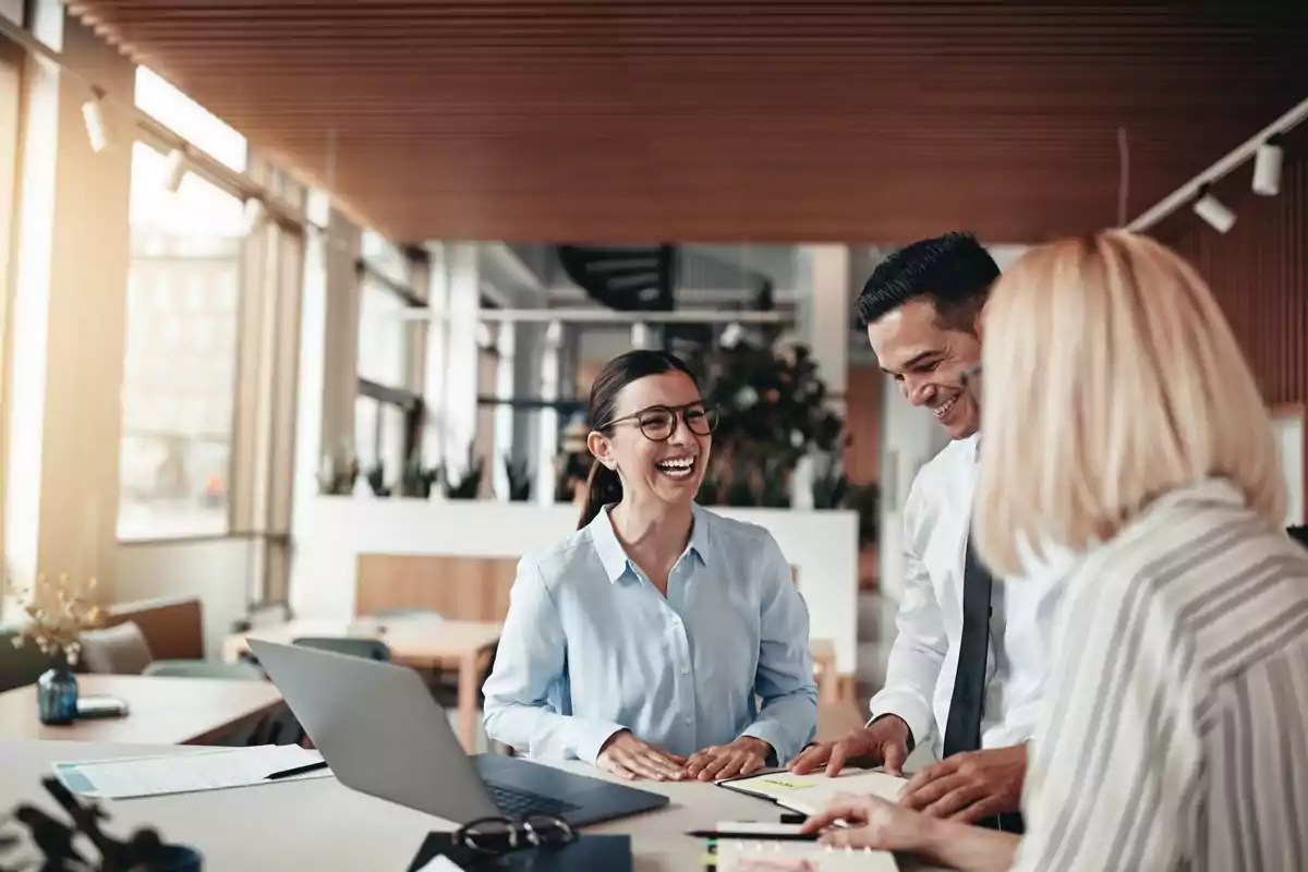 Un grupo de personas sonríe mientras trabaja en una oficina moderna con luz natural y un ambiente colaborativo.