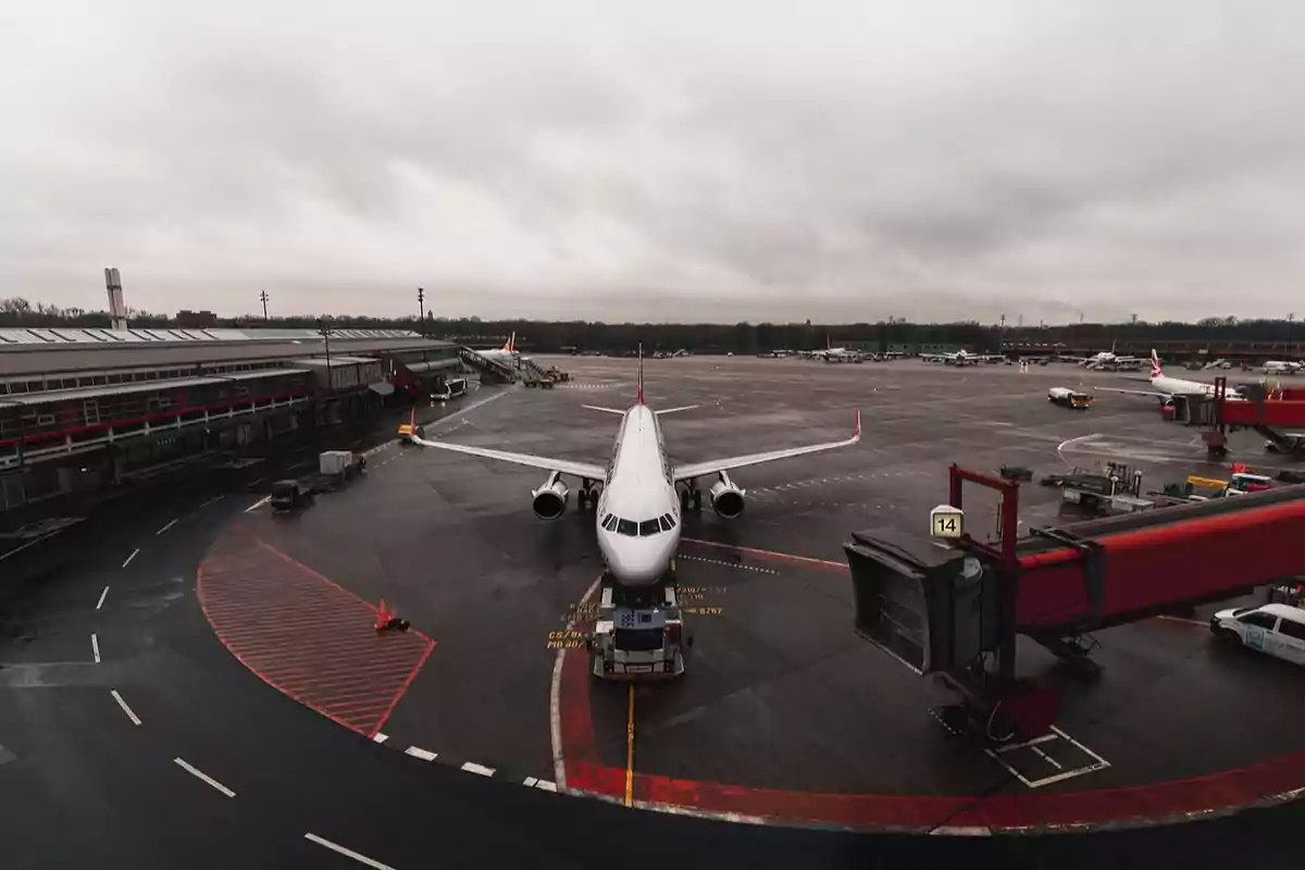 Un avión estacionado en la pista de un aeropuerto con un cielo nublado y edificios terminales al fondo.