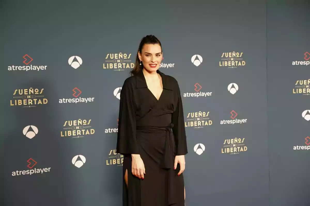 Alba Brunet con vestido negro posando frente a un fondo promocional de 