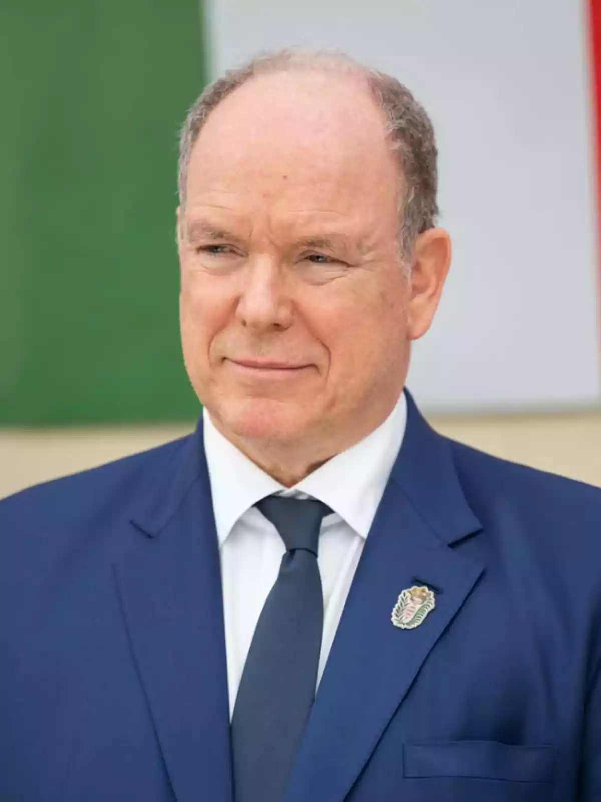Man in a blue suit and dark tie in front of a background with green, white, and red colors. Man in a blue suit and dark tie in front of a background with green, white, and red colors.