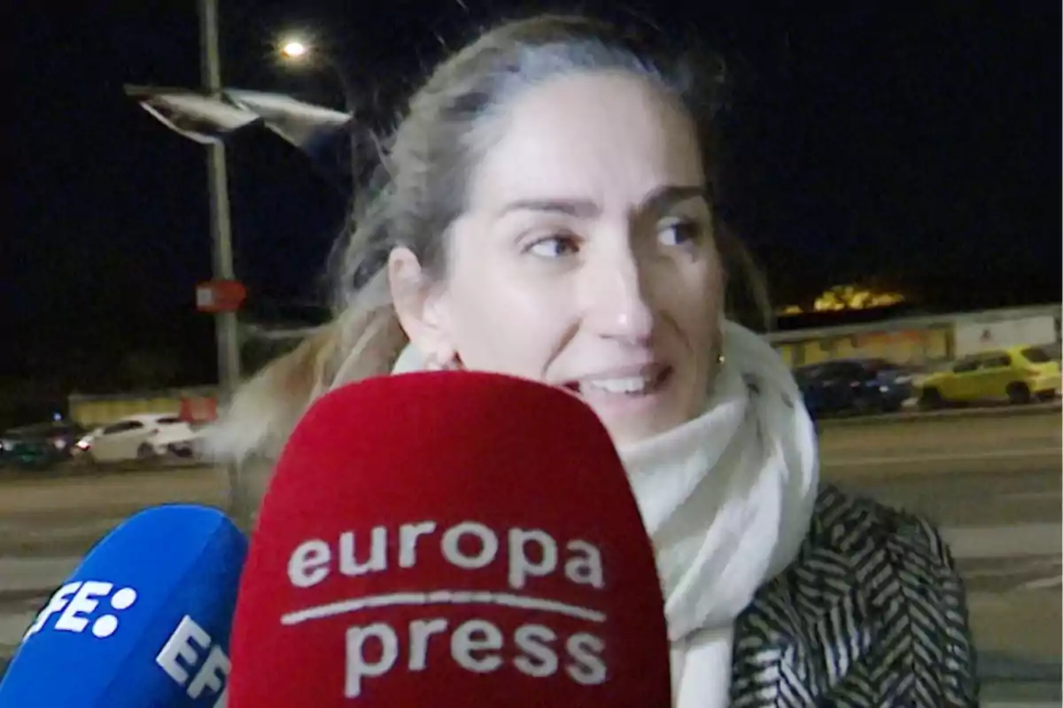 Alejandra Martos con bufanda blanca es entrevistada por medios de comunicación en la calle durante la noche.