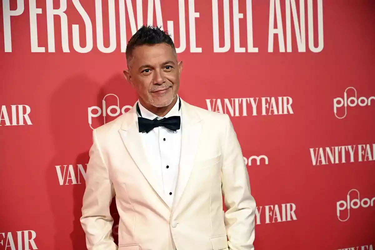 Alejandro Sanz con esmoquin blanco y pajarita negra posando en una alfombra roja con fondo de Vanity Fair Alejandro Sanz con esmoquin blanco y pajarita negra posando en una alfombra roja con fondo de Vanity Fair