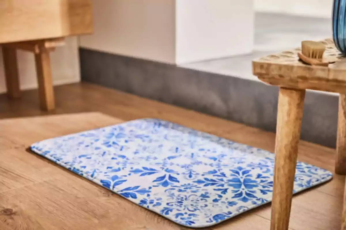 Una alfombra con diseño floral azul sobre un suelo de madera junto a un mueble de madera clara. Una alfombra con diseño floral azul sobre un suelo de madera junto a un mueble de madera clara.