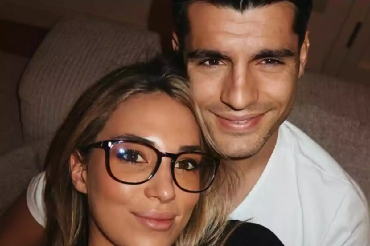 Close-up of Alice Campello and Álvaro Morata smiling and sitting on the couch at home.