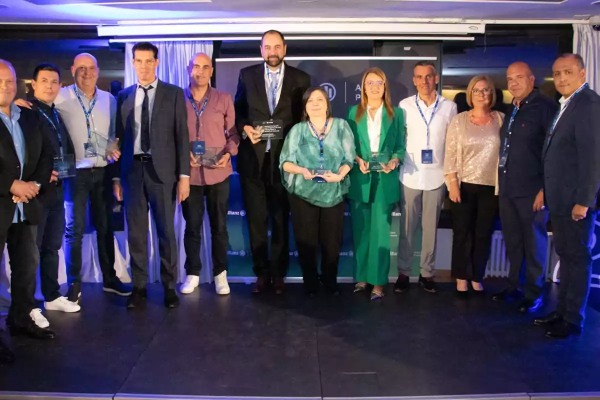 Un grupo de personas posando en un escenario, algunas sosteniendo trofeos, con un fondo que muestra un logotipo de Allianz.