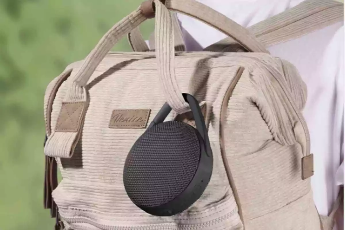 Una mochila beige con un altavoz portátil negro colgado de una de sus asas. Una mochila beige con un altavoz portátil negro colgado de una de sus asas.