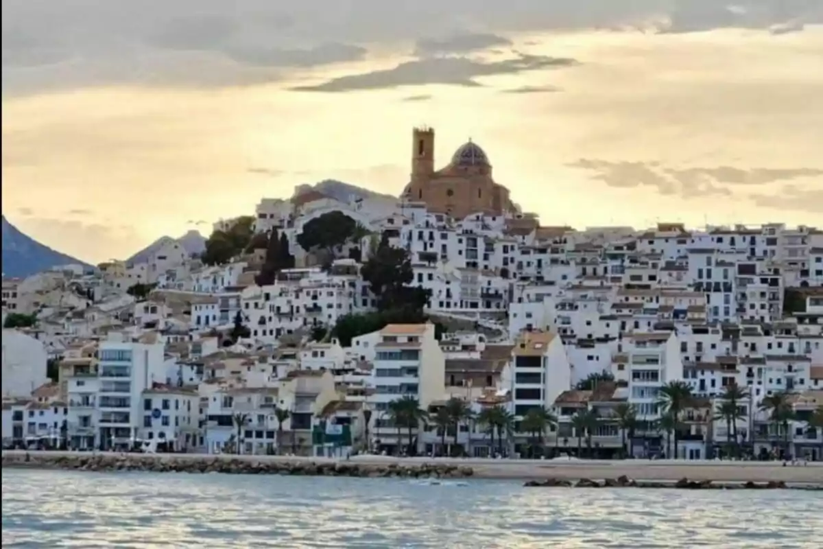 Vista panorámica de un pueblo costero con casas blancas y una iglesia en la cima al atardecer.